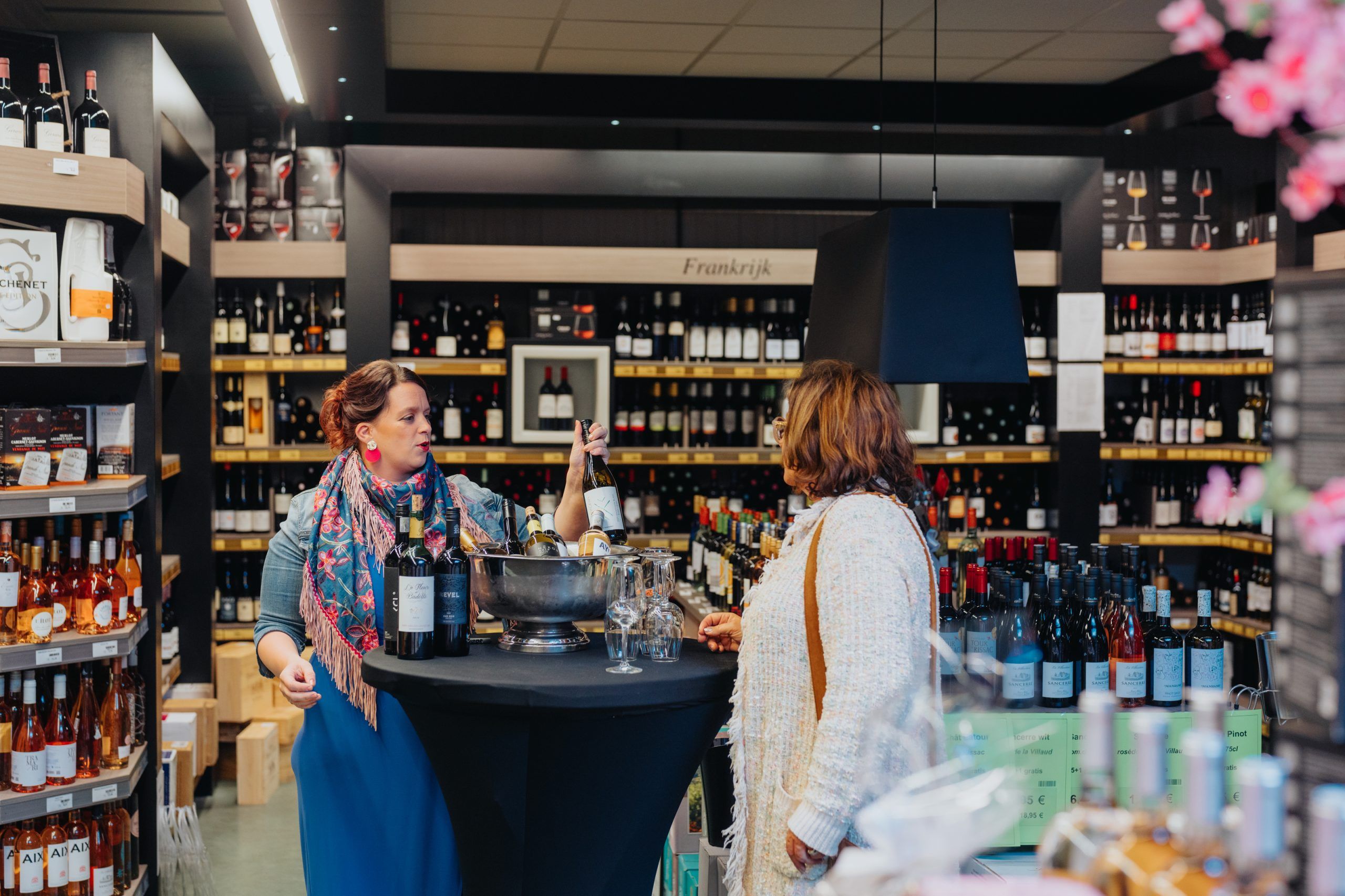 Een medewerkster van Kempendrinks toont een fles wijn aan een klant tijdens een proeverij in de winkel.