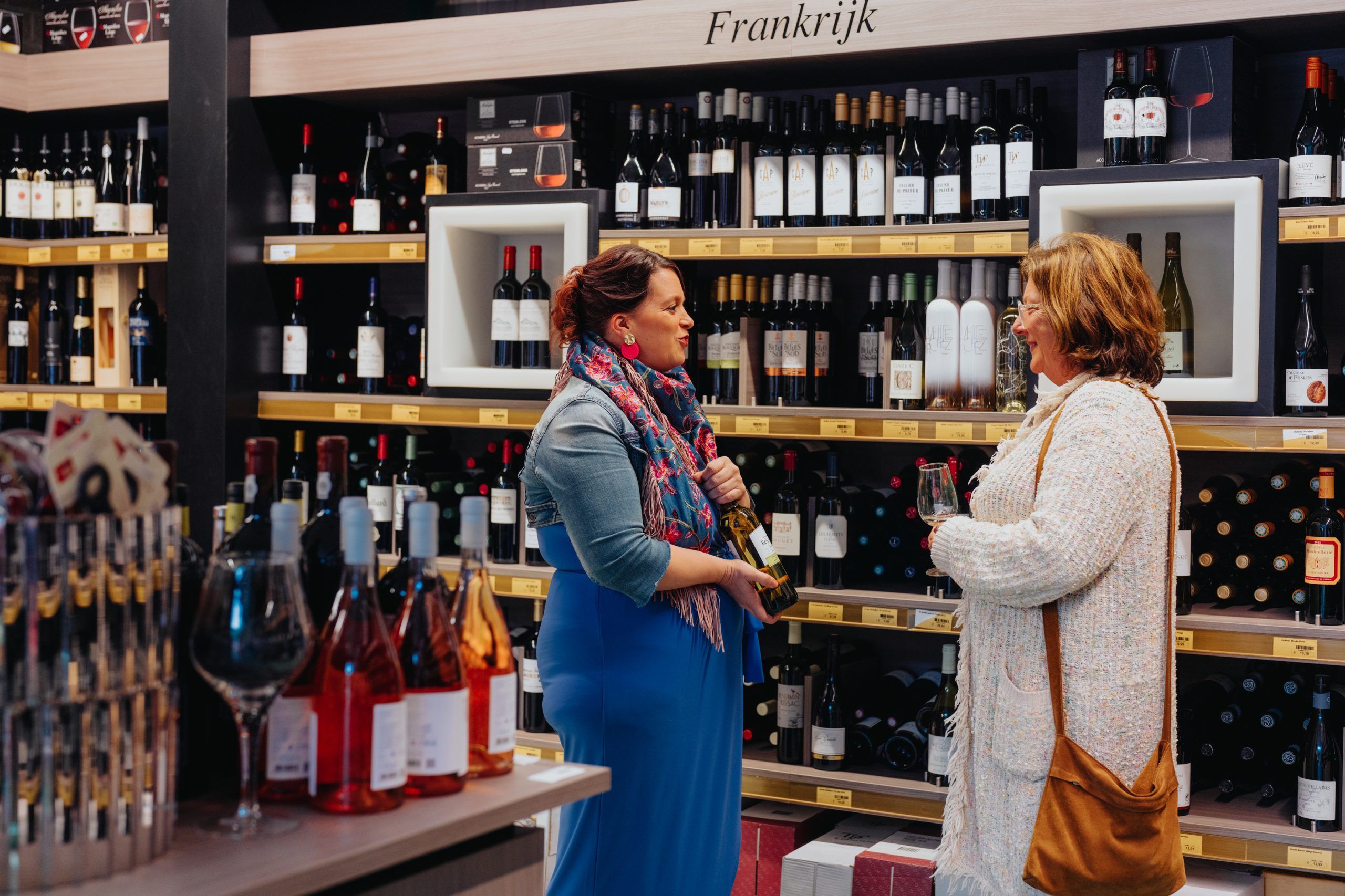 Een klant en medewerkster lachen tijdens een gesprek in de wijnwinkel.