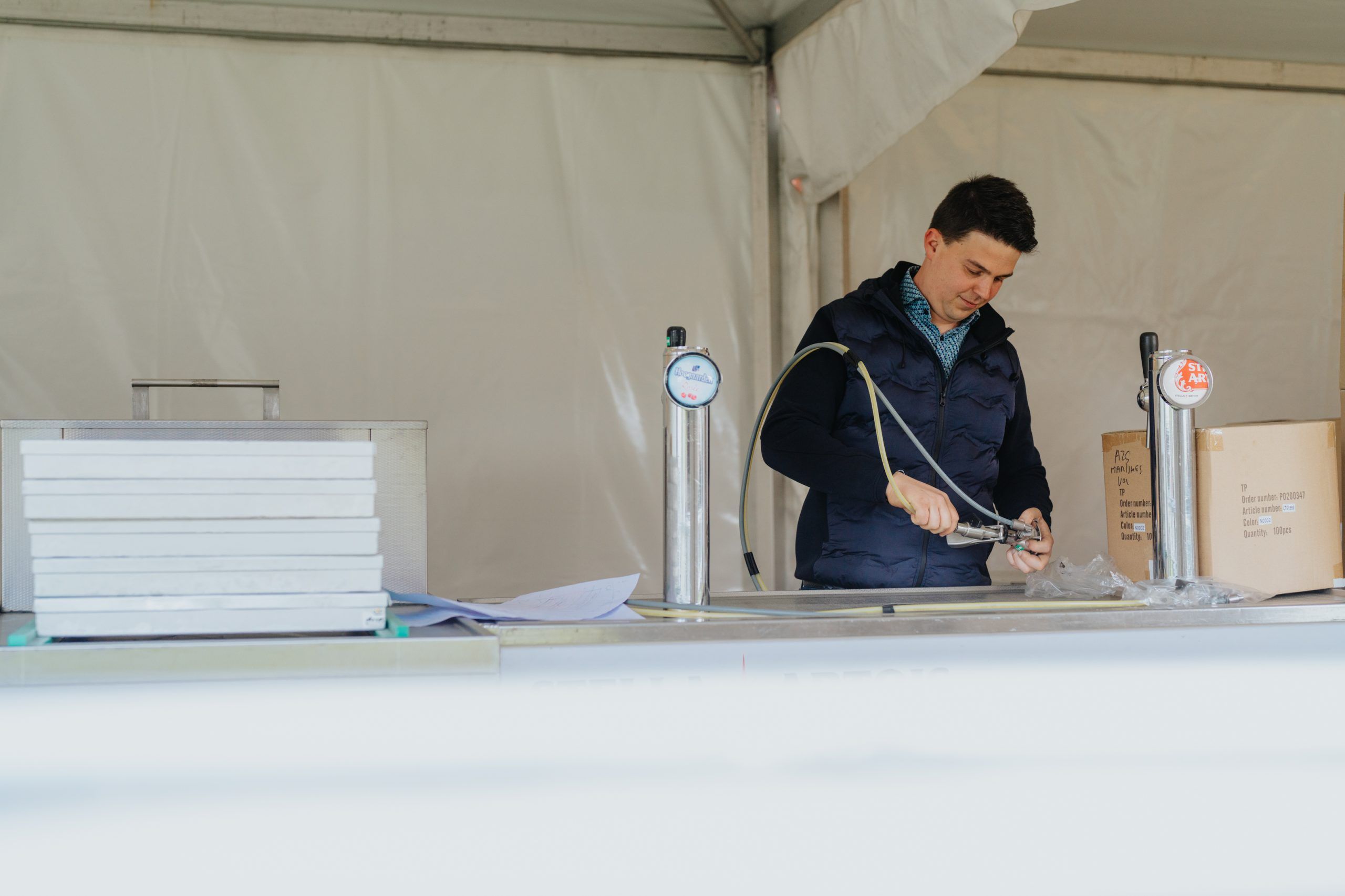 Medewerker bevestigt een biertapslang in een festivaltent.